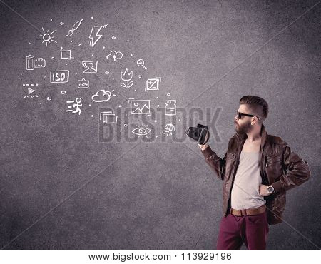 An elegant hipster guy trying to use a vintage camera with camera settings icons drawn on wall, like flash, white balace or ISO value concept