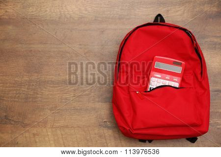 Backpack and calculator on wooden background