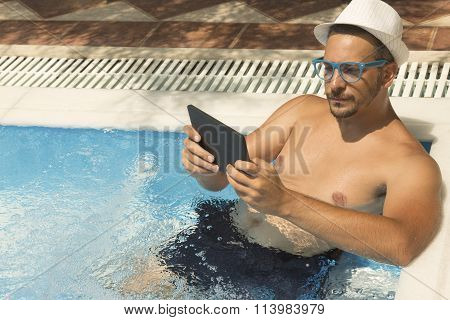 Young guy using tablet device while relaxing in the swimming pool