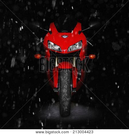 KRASNOYARSK RUSSIA - OCTOBER 15 2017: Red sports bike in the dark in the winter. Snowing flakes. Winter storage of a motorcycle. Two lights. Front view. Isolated on a black background.