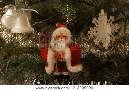 A small Santa Claus was hung on in the fir tree, on one side there are small bells and on the other side flake of Christmas. Front view. Indoor shooting and without character, artificial light.