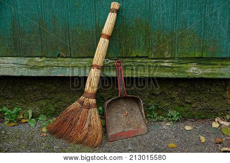 old broom and dirty scoop near the wooden green wall