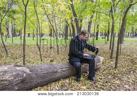 Businessman Having A Laptop In The Park In The Fall. A Man Is Working At A Computer In The Park.