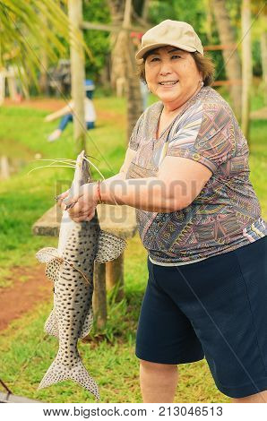 Elderly Fisherwoman Holding A Pintado Fish, Looking Forward And Smiling.