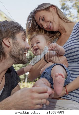A young beautiful couple are teesing their happy woughing cute baby.