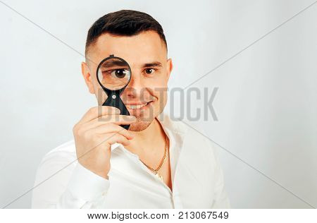 A young man is holding a magnifying glass near his eyes. The concept of information retrieval