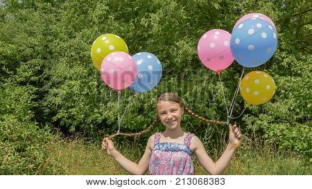 Cheerful and pretty girl with colorful balls attached to her hair and braids on her head. Funny idea with balloons