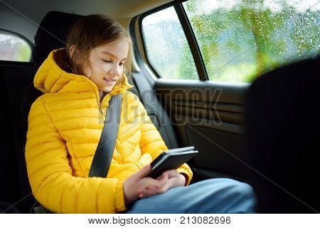 Adorable Girl Sitting In A Car And Reading Her Ebook On Rainy Autumn Day. Child Entertaining Herserf