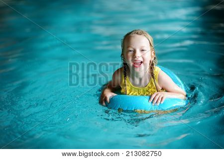 Cute Little Girl Playing With Inflatable Ring In Indoor Pool. Child Learning To Swim. Kid Having Fun