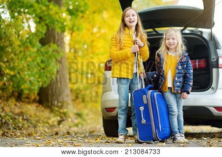 Two Adorable Girls With A Suitcase Going On Vacations With Their Parents. Two Kids Looking Forward F