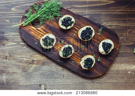 Top view of black caviar appetizers at wooden board