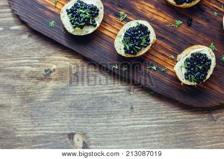Top view of black caviar appetizers at wooden board