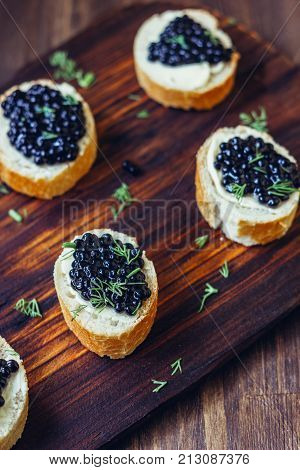 Black caviar on the pieces of bread over wooden kitchen board