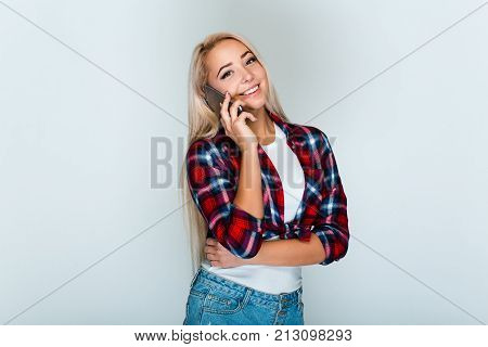 Great phone call! Beautiful young woman with blond hair talking on mobile phone and
looking at camera with smile while standing against grey background
