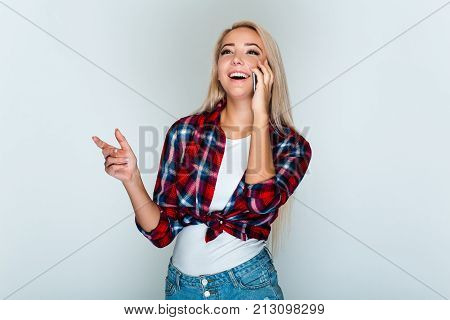 See you on a party! Beautiful young woman with blond hair talking on mobile phone and
looking away with smile while standing against grey background