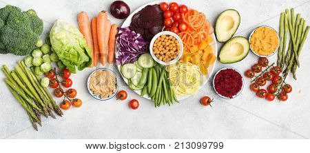 Healthy eating concept, above view of rainbow buddha bowl, various vegetables, carrot, courgette, cabbage, chickpeas, cucumber and tomatoes, on wooden board on white table, long photo, selective focus