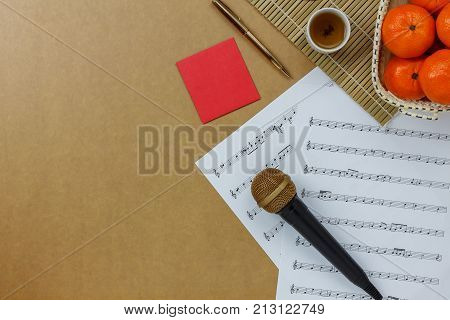 Table top view of music sheet note and accessories Chinese new year & Lunar festival concept.Essential items on modern rustic brown wooden at home office desk.Orange in basket with tea and red pocket.