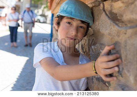 Portrait of a boy in a T-shirt and a cap near the stone wall.