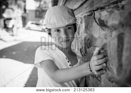 Portrait of a boy in a T-shirt and a cap near the stone wall. Black and white.