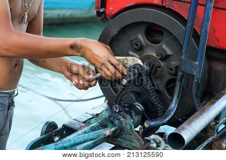 Men are repairing engines adapted for long-tail boats. Maintenance the chain gear and equipment for modified old diesel engine and spare parts in Thailand.