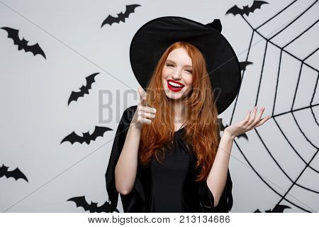 Halloween Witch Concept - Happy Halloween Witch Pointing Finger On Side Over Dark Grey Studio Backgr