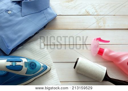 Laundry tool set with blue shirt and electric iron on white wooden table for copy space