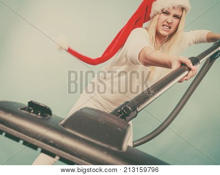 Woman vacuuming the house last minute. Teen girl in santa helper hat with vacuum cleaner angry furious face expression. Christmas time and housework concept.