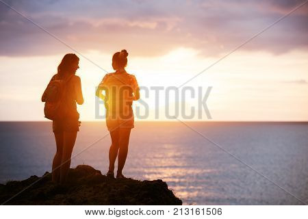 Travel concept with two girls backpachers on sea sunset background