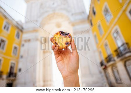 Holding portuguese egg tart pastry called pastel de Nata outdoors on the triumphal arch background in Lisbon