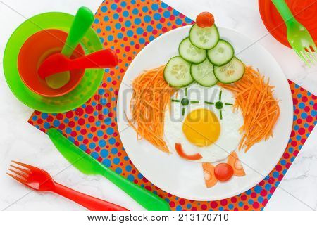 Dinner or breakfast for kids - fried egg with vegetables in the shape of clown face. Creative food art idea for children meal top view