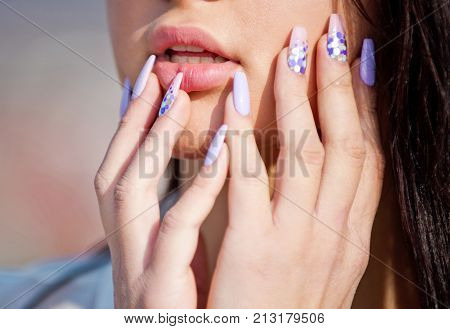 Female hands touch her face fashion manicure for the girl healthy hands and nails pink and purple colors in the trend of the season. Girl touches her sexy lips with her nails part of the face