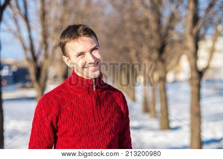Portrait of handsome young man in red in a sunny snowy day. Winter lifestyle portrait of handsome young man walking in the snowy park