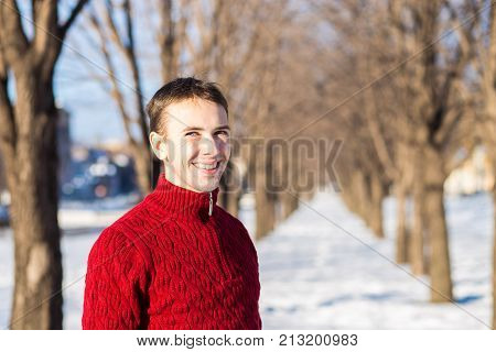Portrait of handsome young man in red in a sunny snowy day. Winter lifestyle portrait of handsome young man walking in the snowy park