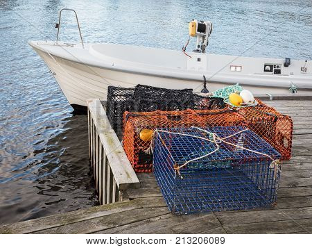Traps for lobster and crabs standing on pier next to a white motor boat.