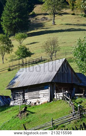 The Old Ukrainian Hut With A Slate Roof And A Wooden Fence In A Green Field