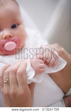 A newborn baby with a delicate pink skin lying on her mother's lap with a pink pacifier in her mouth, Mom gently holds the handle of her son, the child clamps the pens of the jaws, the ring on the mother's finger