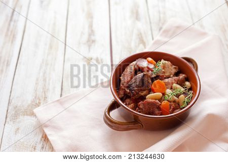 Cassoulet. Containing meat pork sausages goose duck and sometimes mutton and two types of white beans. French food cuisine. On old wooden white background.