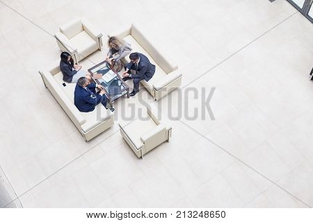 Directly above view of concentrated group of colleagues gathered together at spacious office lobby and brainstorming on joint project