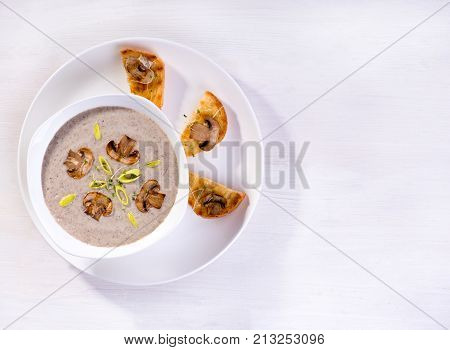 Soup with champignons leek and crispy croutons on white background top view.
