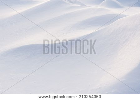 Abstract winter background. Play of light and shadow on undulating slopes of white snowdrifts.