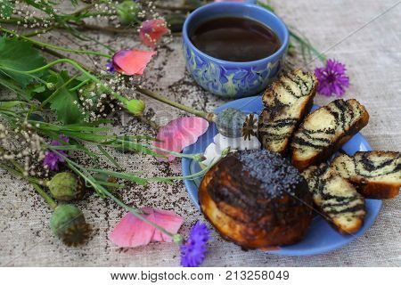 Sweet bun with flax seed and poppy and cup of tea on table.
