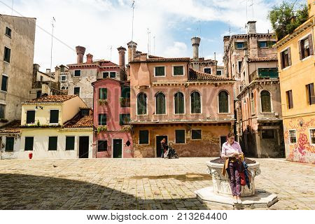 A Tourist Reads A Guide While She Is Leaning Against A Well In A Square In Venice