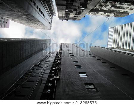 Huge grey skyscrapers are around and only above blue sky and clouds. View from ground upward