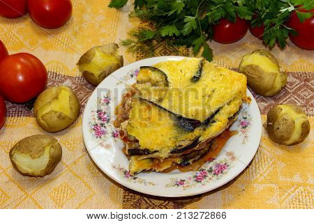 Hot Ready Moussaka Is Served On A Porcelain Plate Among Vegetables And Spicy Herbs. Fresh Vegetables