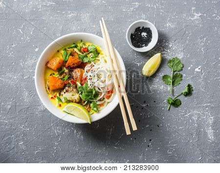 Vegan khao soi soup on a grey background top view. Vegetarian soup with turmeric rice noodles baked pumpkin and cauliflower. Healthy food concept