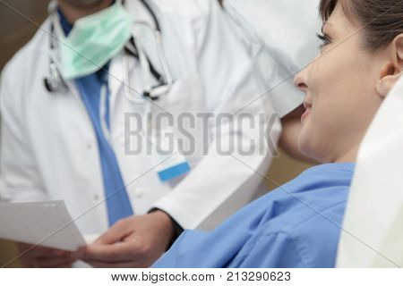 A smiling pretty female patient is listening to her diagnosis held by a doctor, torso only, blurred in background.