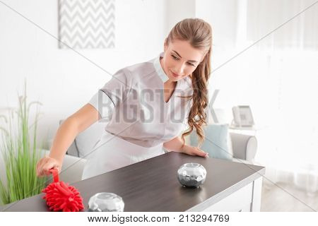 Chambermaid cleaning table from dust in room