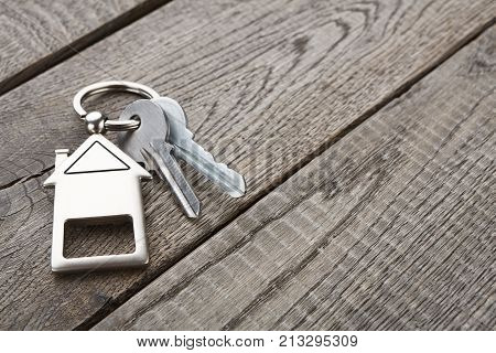 Two steel keys with house shaped trinklet on keyring on wooden background with copy space. Home key, safety, security, real estate and rent concept