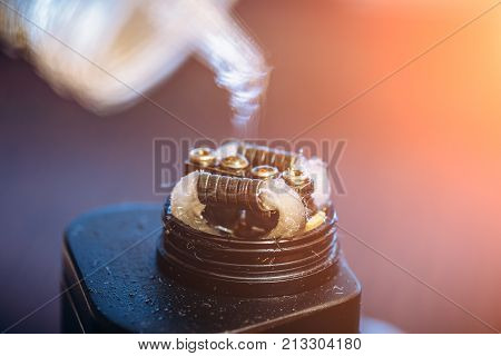 Rebuildable dripping atomizer or RDA for vaping or e-cigarette with Alien Clapton coil and cotton stripes wetted with e-liquid, modern vape device for quit smoking, macro photo with selective focus