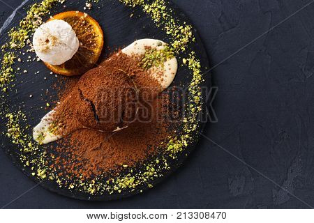 Exquisite dessert on black background. Chocolate fondant, creme anglaise and vanilla ice cream, sprinkled with cocoa on slate decorated with orange citron and pistachio crumble, top view, copy space